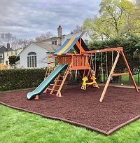 A wooden playground set with a slide and swings in a backyard.