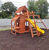 A wooden playground with a yellow slide and stairs in a backyard.
