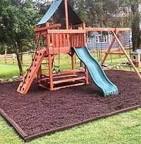 A wooden playground with a slide and swings in a yard.