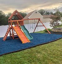 A wooden playground with a slide , swings , and stairs in a backyard.