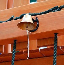 A bell is hanging from the side of a wooden structure.