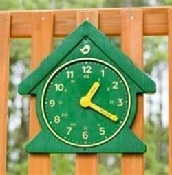 A green clock is hanging on a wooden fence.