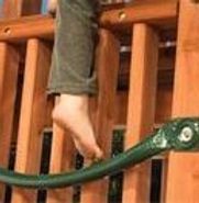 A person is standing on a green hose attached to a wooden fence.