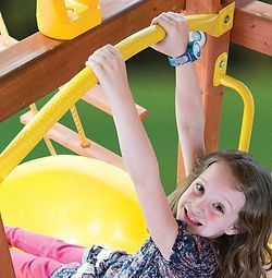 A little girl is playing on a yellow swing set.