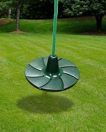 A green disc swing is hanging from a rope in the grass.