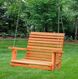 A wooden porch swing is hanging from chains in a grassy yard.