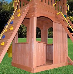 A wooden playhouse with a slide and stairs is sitting on top of a lush green field.
