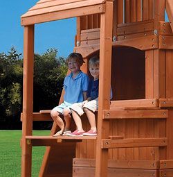 Two young boys are sitting on top of a wooden playset.