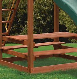 A wooden picnic table is sitting in the grass next to a slide.