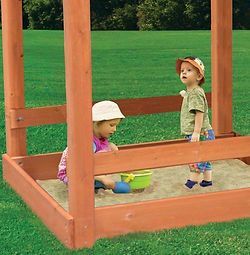 Two children are playing in a wooden sandbox.