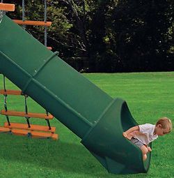 A young boy is going down a green slide on a playground.