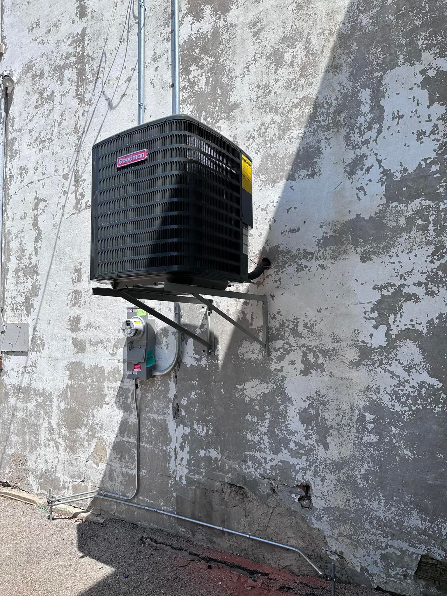 Wall-mounted black air conditioner unit on a weathered concrete exterior wall.