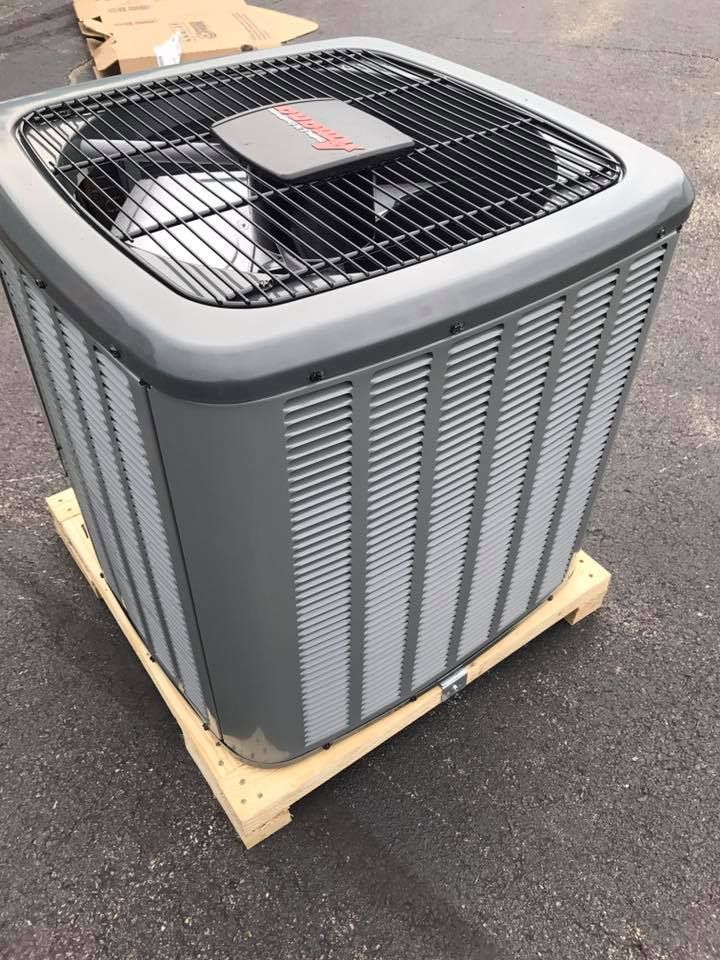 Outdoor air conditioning unit on a wooden pallet, with a gray metal housing and black top grille.