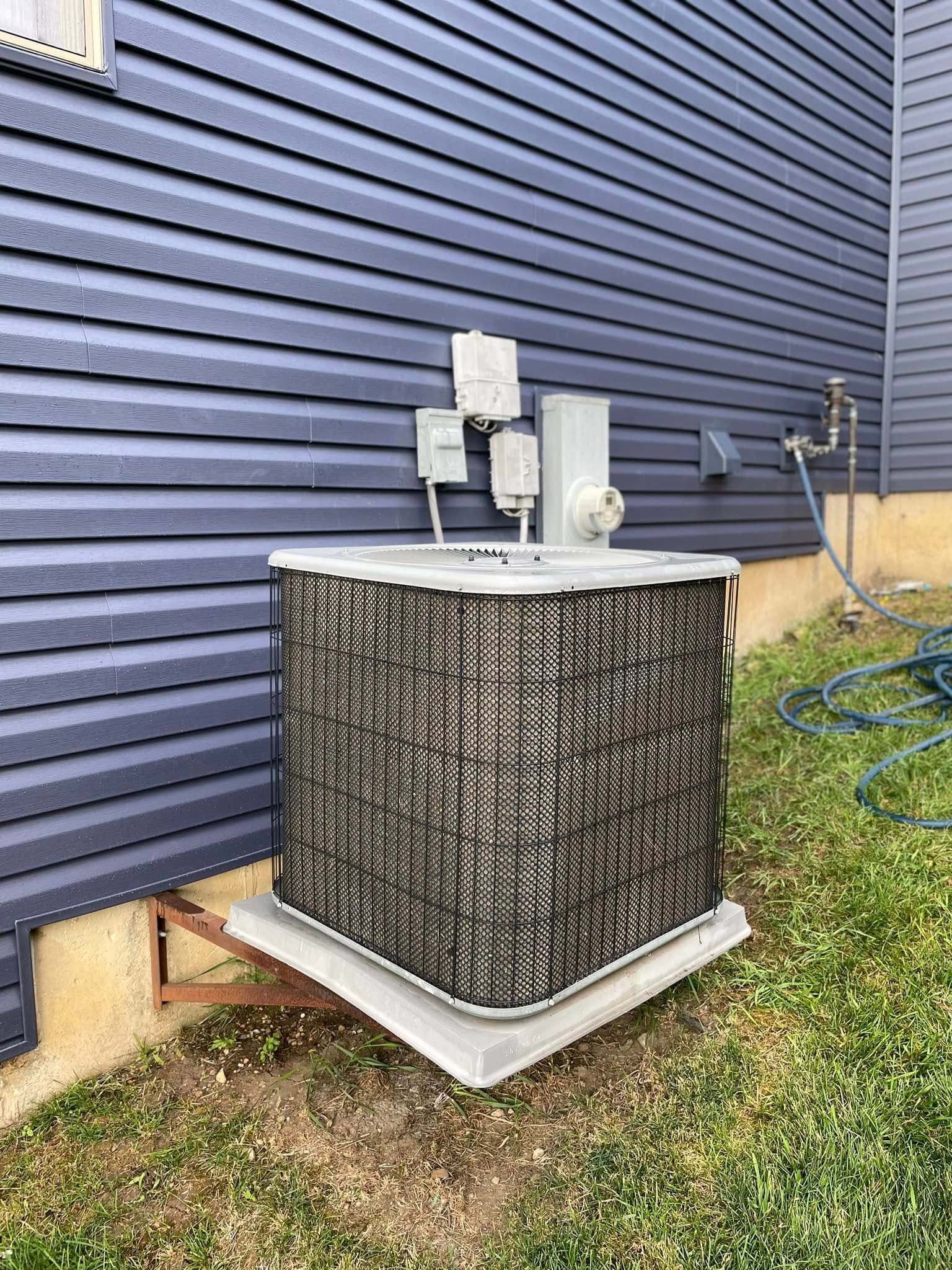 Outdoor air conditioner unit beside a blue house wall, with a black protective cover and snow on top.