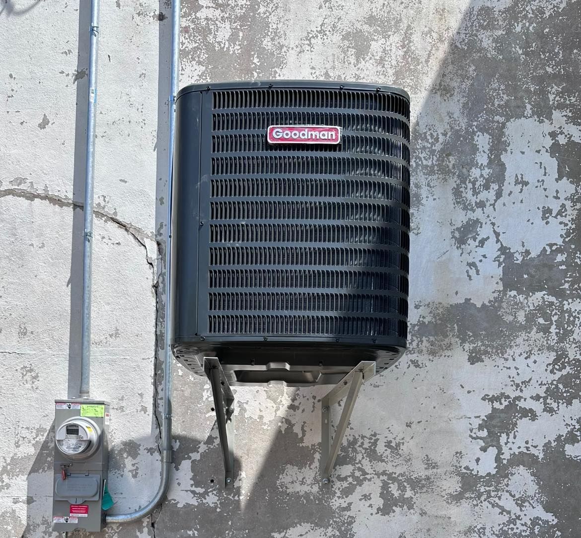 Black wall-mounted Trane HVAC unit on a weathered exterior wall with utility meter below