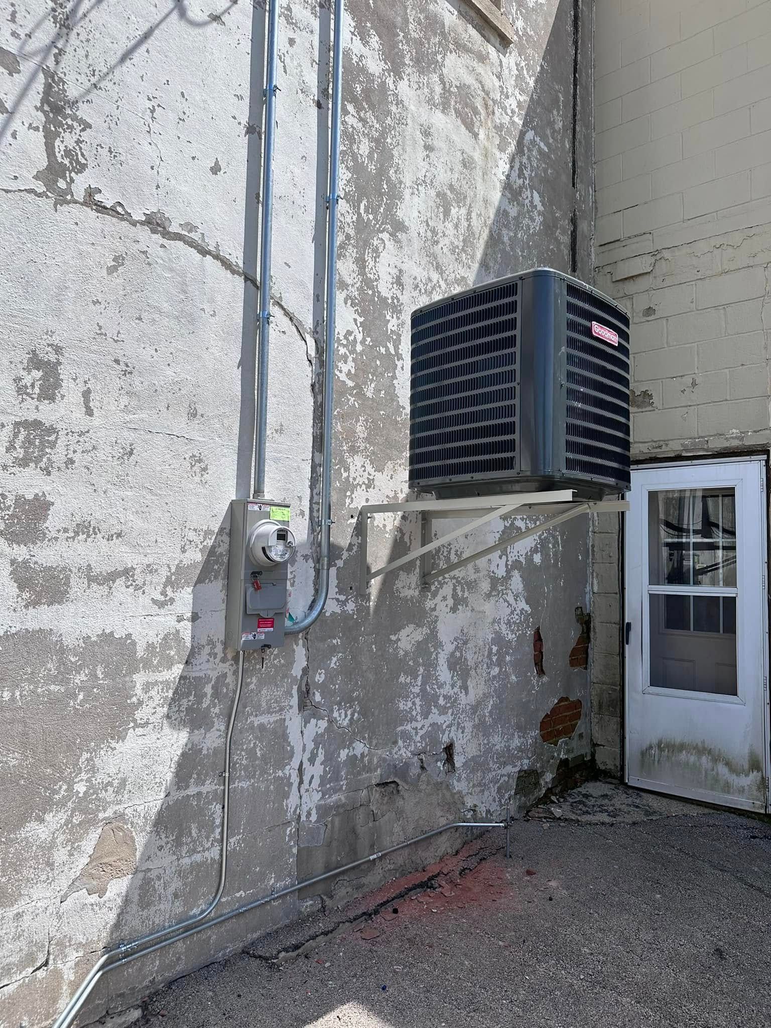 Exterior wall with utility pipes and a mounted HVAC unit beside a door