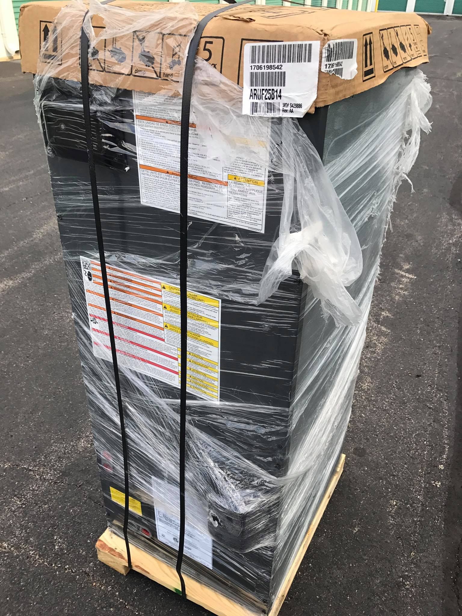 Wrapped pallet of boxed goods strapped with black bands on a wooden pallet outdoors.