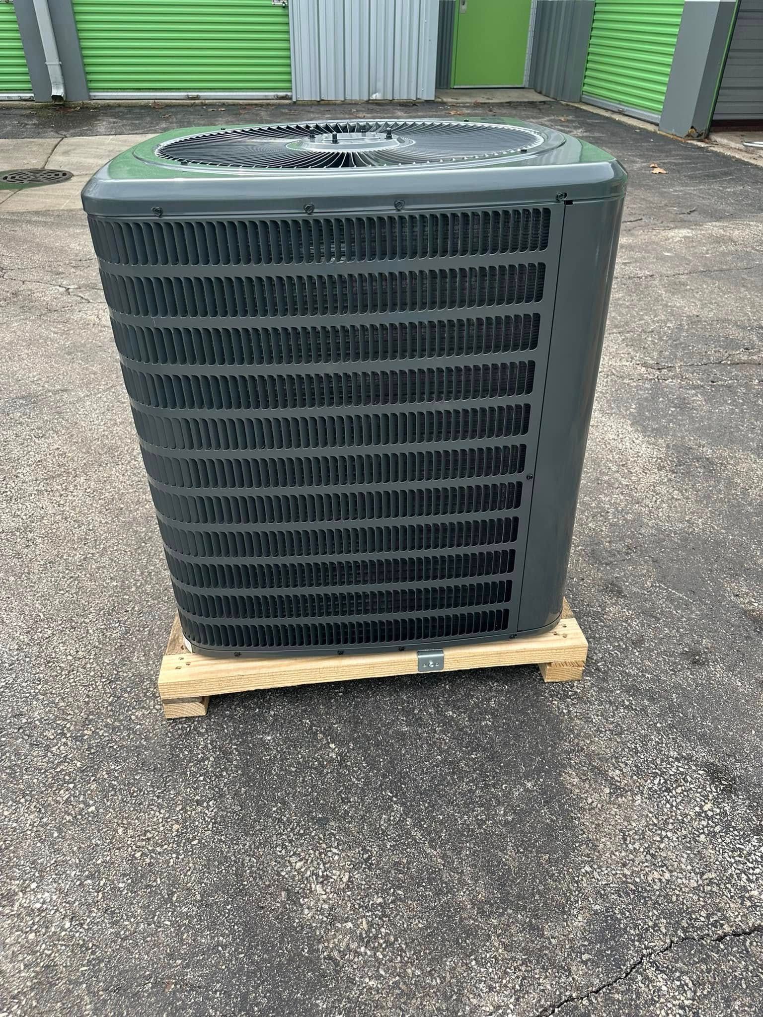 Large black HVAC unit on a wooden pallet outdoors in front of green storage doors