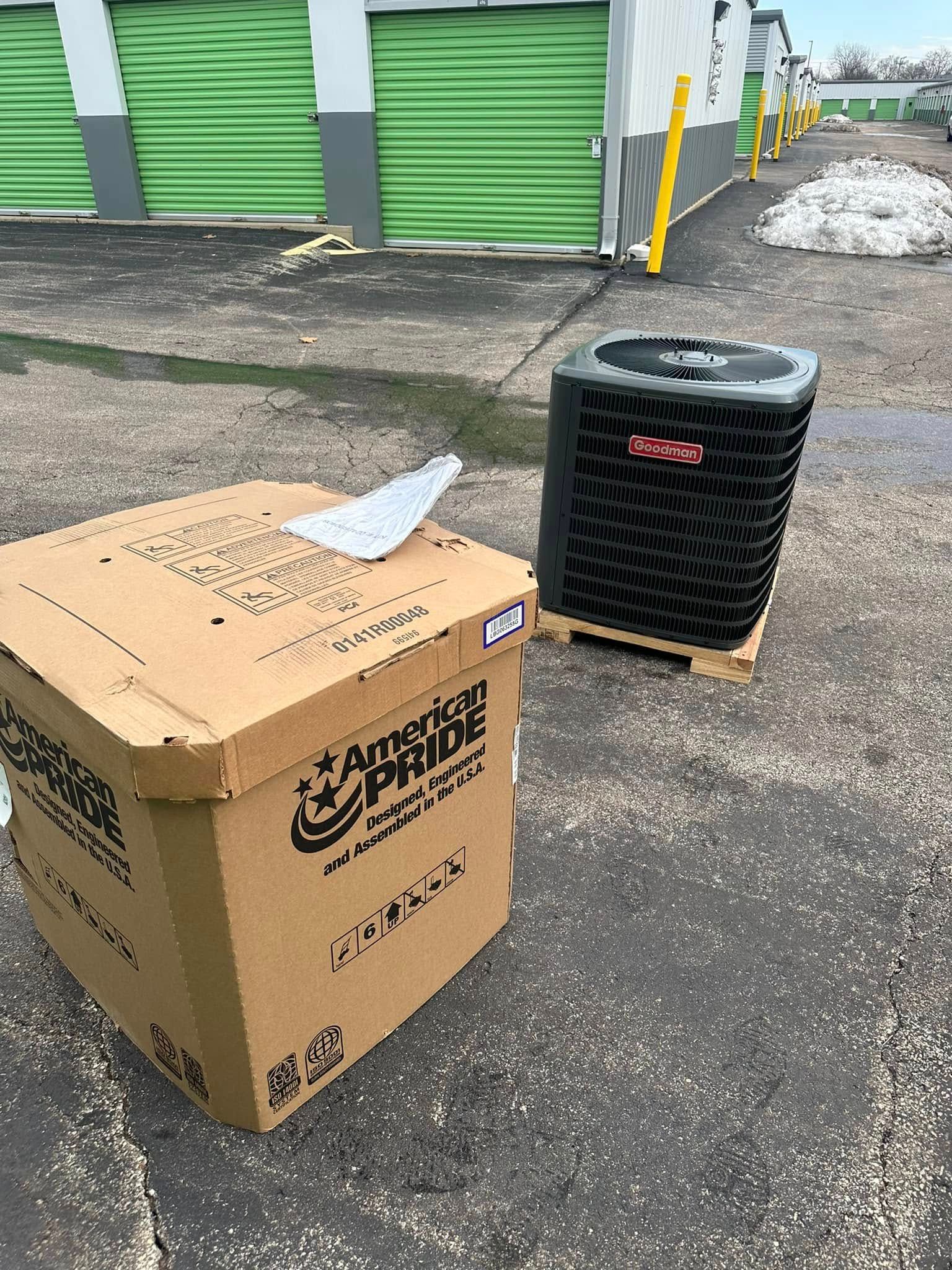 Cardboard box and black HVAC unit on pavement in front of green storage unit doors