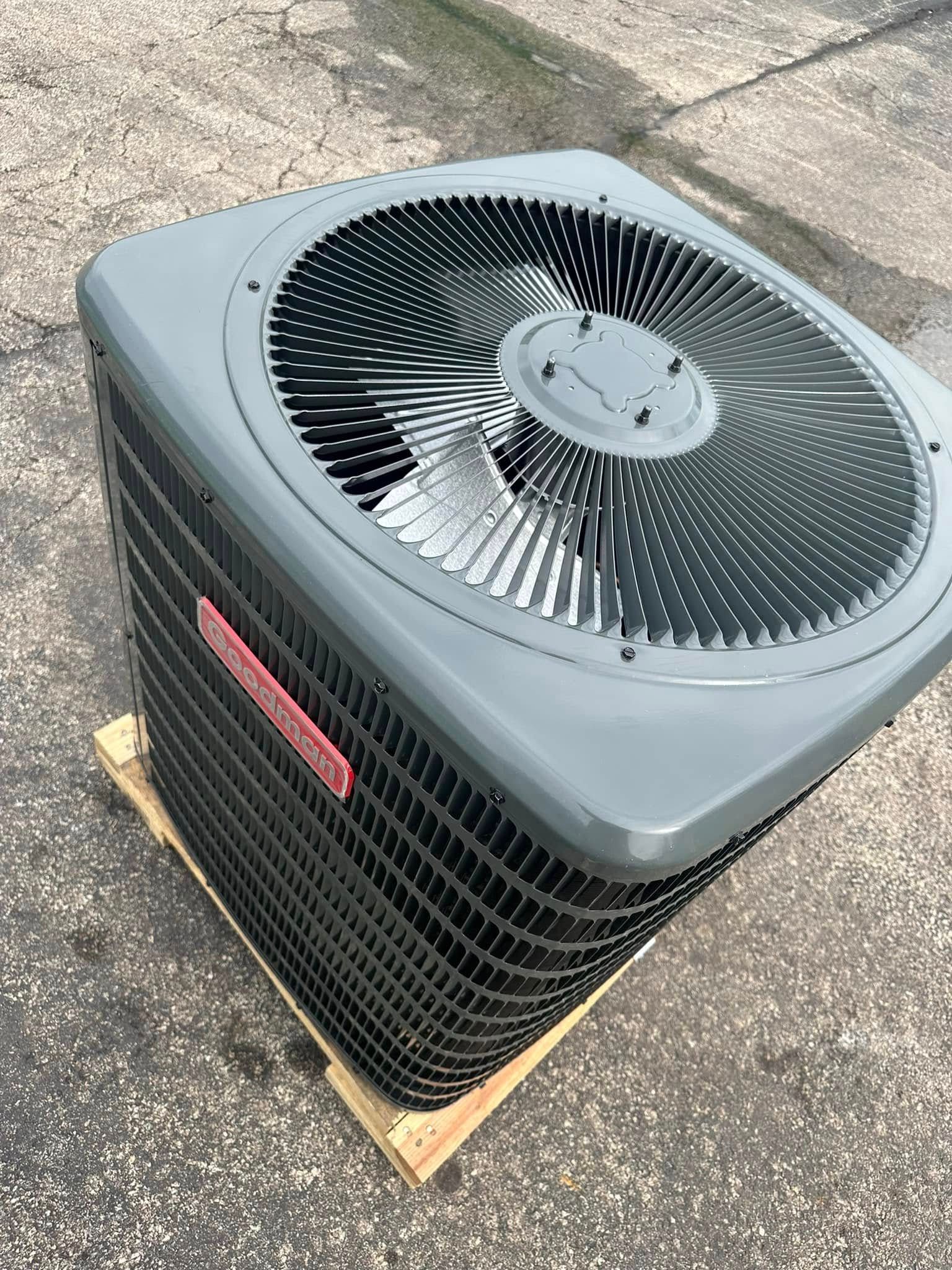 Outdoor HVAC unit on a wooden base on pavement, with a black top fan and gray housing