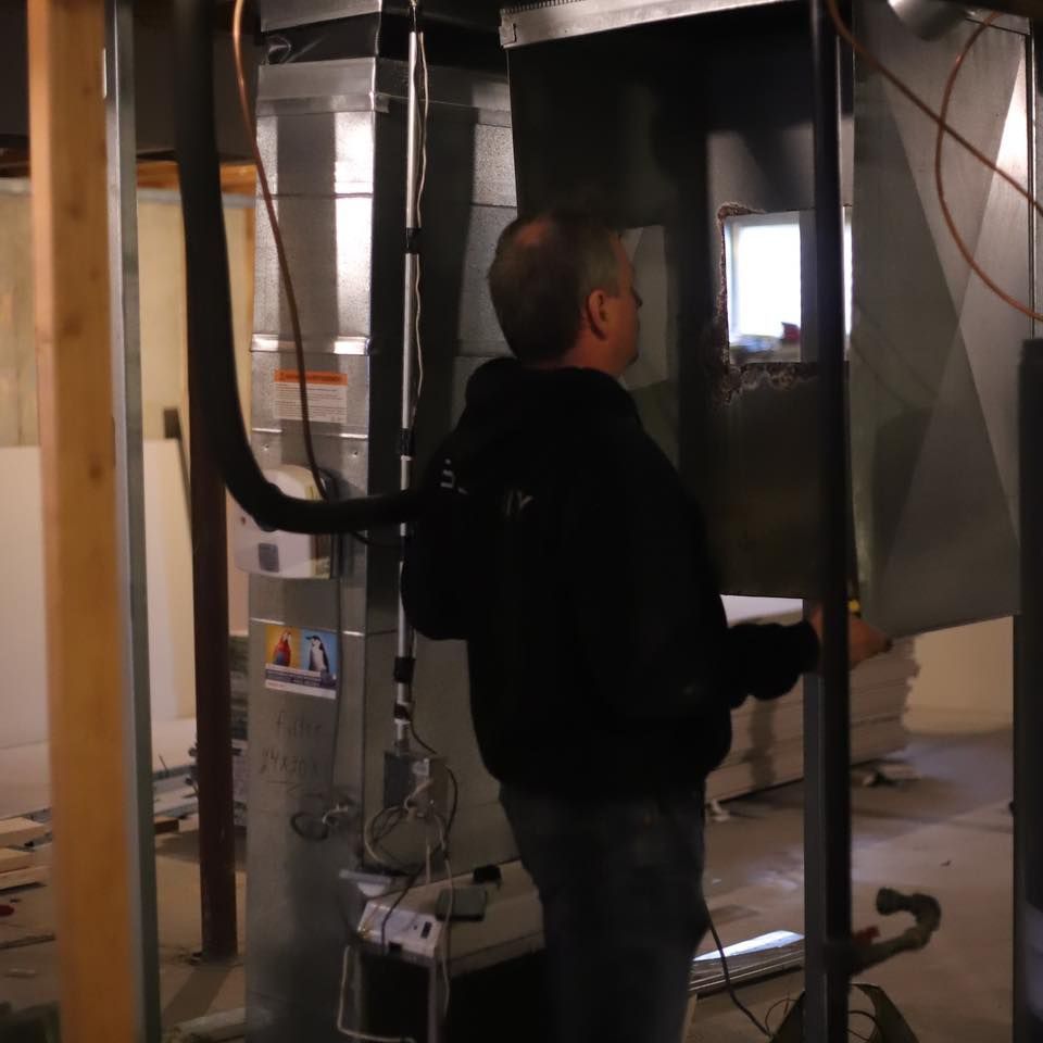 Man inspecting HVAC ductwork in a partially finished room with exposed framing and wiring
