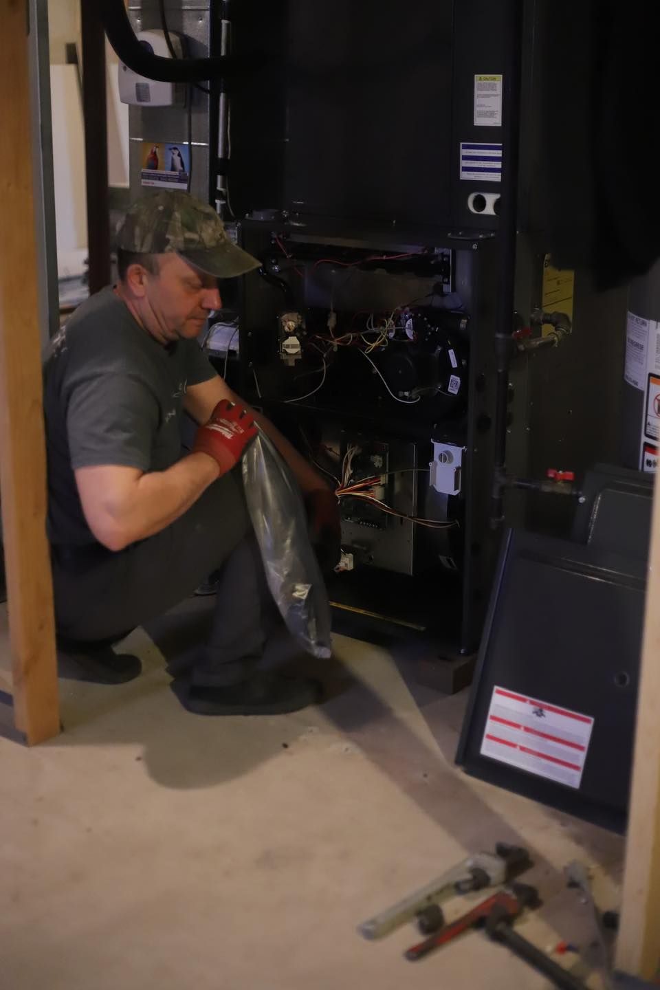 Technician kneeling inside an open machine cabinet, inspecting wiring with tools on the floor nearby.