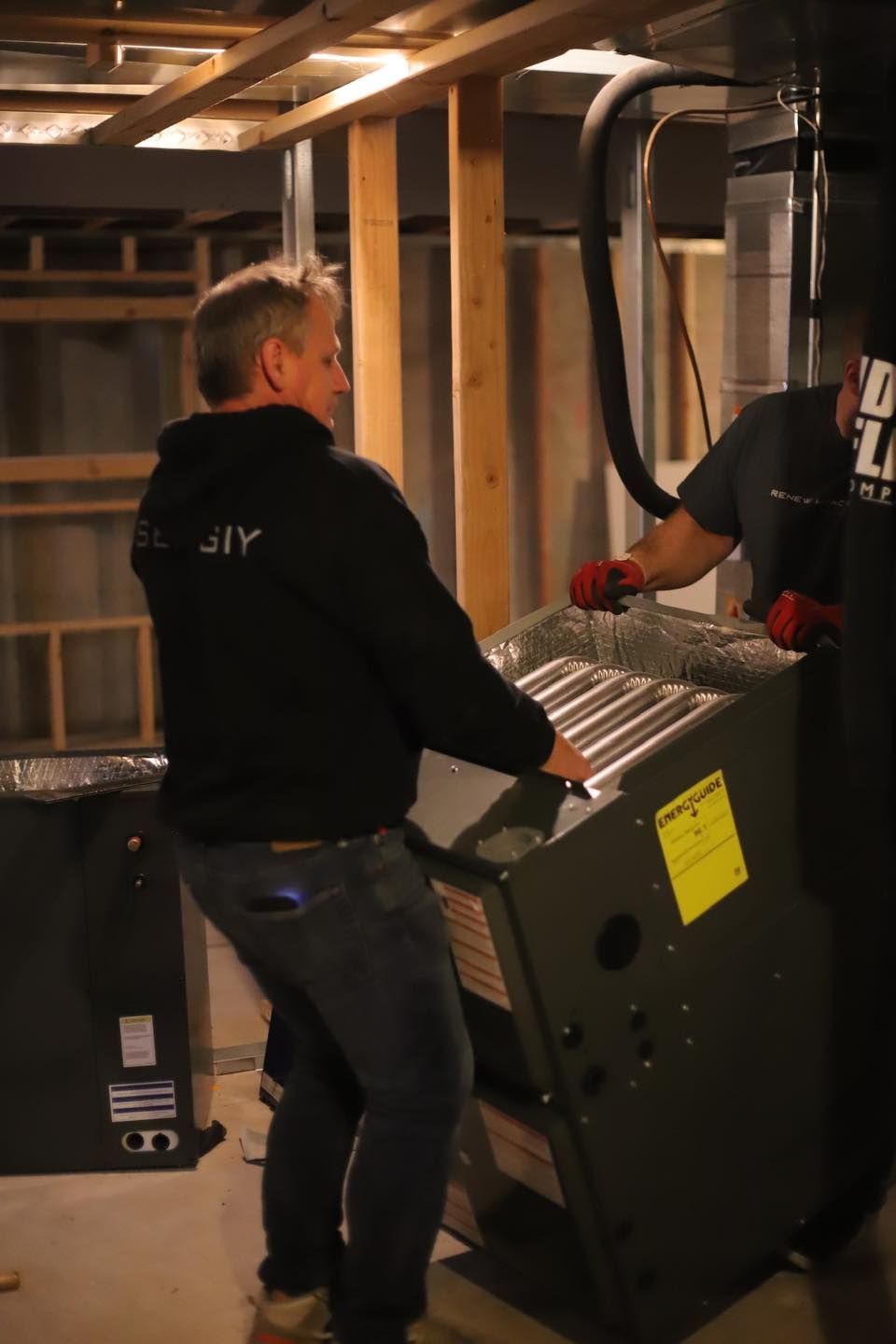Two workers moving a large metal appliance in a basement with exposed beams