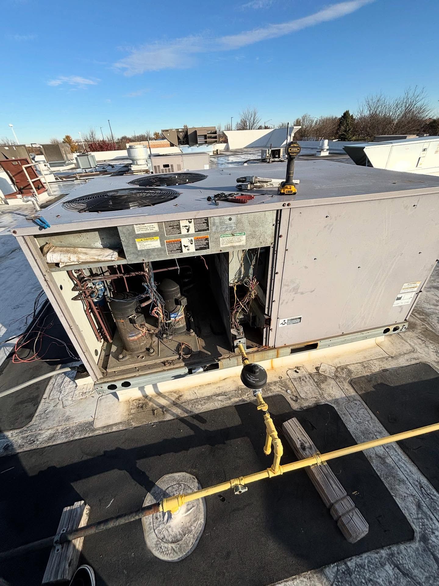Damaged rooftop HVAC unit with exposed wiring and open panel on a snowy roof