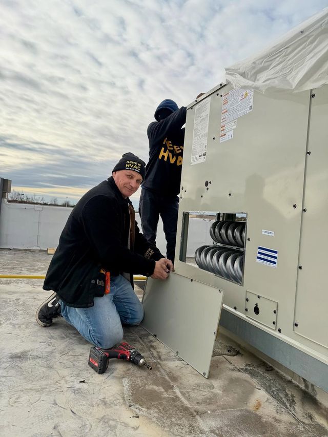 Technicians crouch beside a large outdoor HVAC unit on a rooftop under a cloudy sky.
