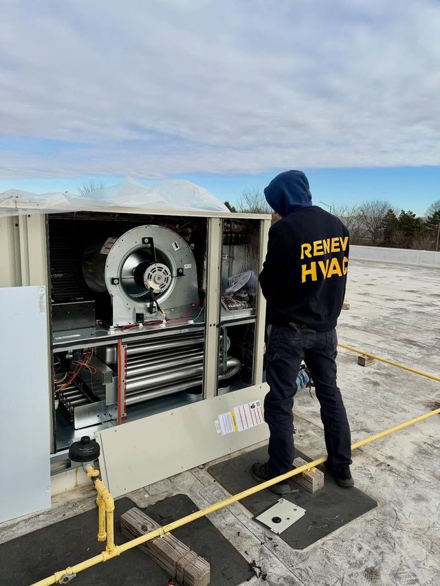 Worker in black hoodie inspecting outdoor industrial machinery on a snowy rooftop.