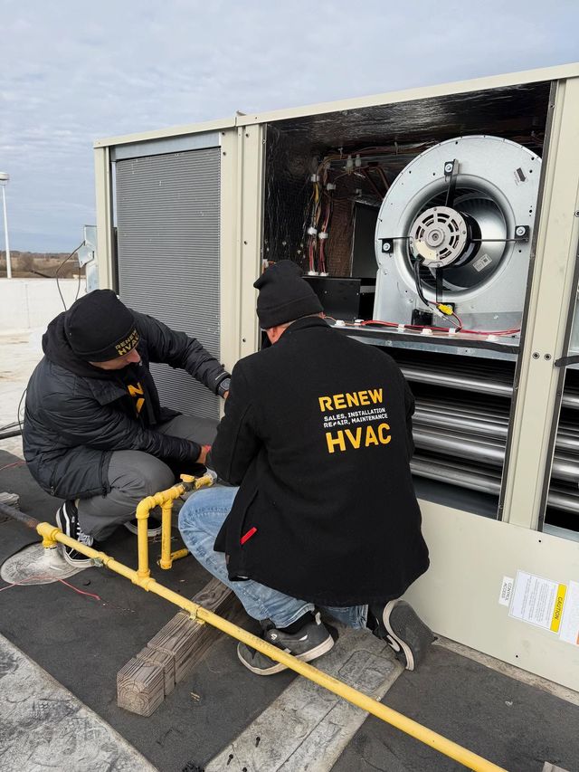 Two HVAC technicians kneel beside a rooftop unit, inspecting the exposed fan and components.