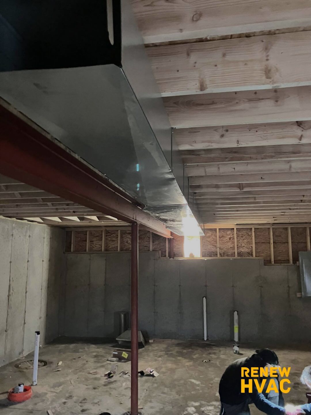 Basement under construction with exposed joists, concrete walls, metal ductwork, and daylight through an opening