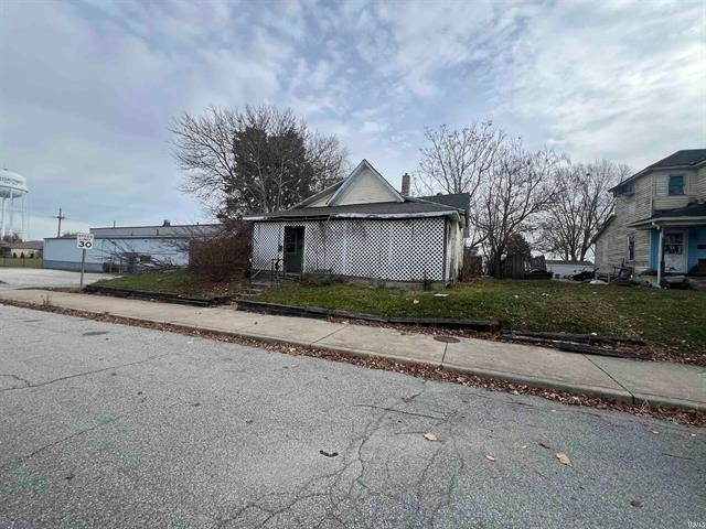 A small white house is sitting on the side of the road next to a sidewalk