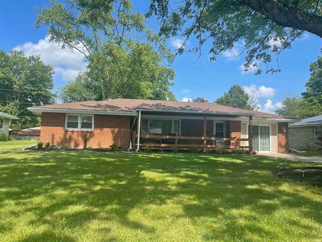 A brick house with a porch and a large lawn in front of it