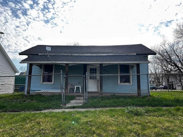 A small blue house with a porch and a fence in front of it