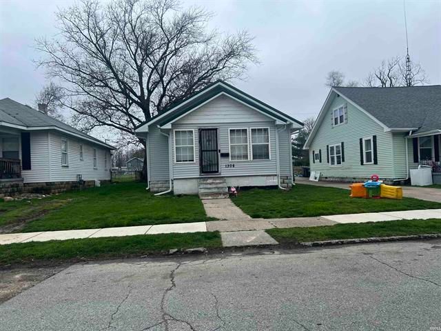 A small white house is sitting on the corner of a residential street