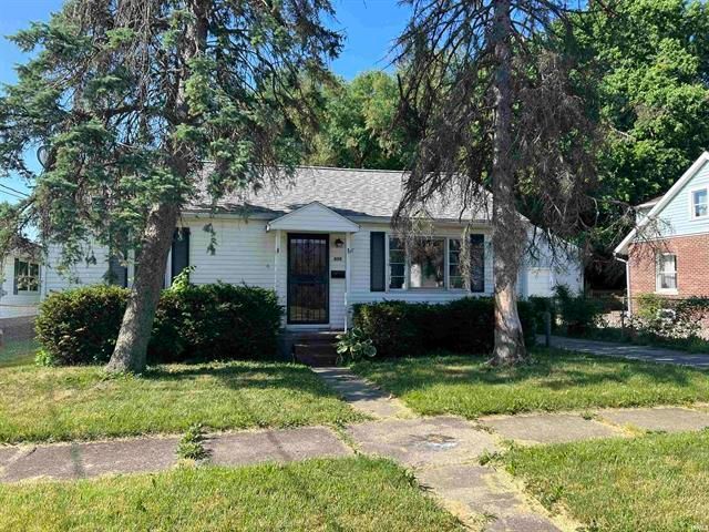 A white house with a gray roof is surrounded by trees and grass