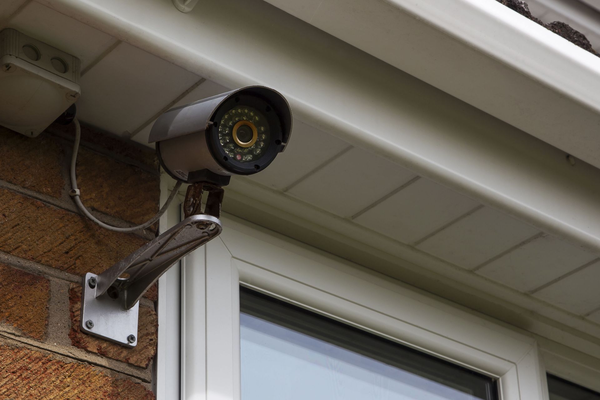 Outdoor security light mounted under a house eave above a window