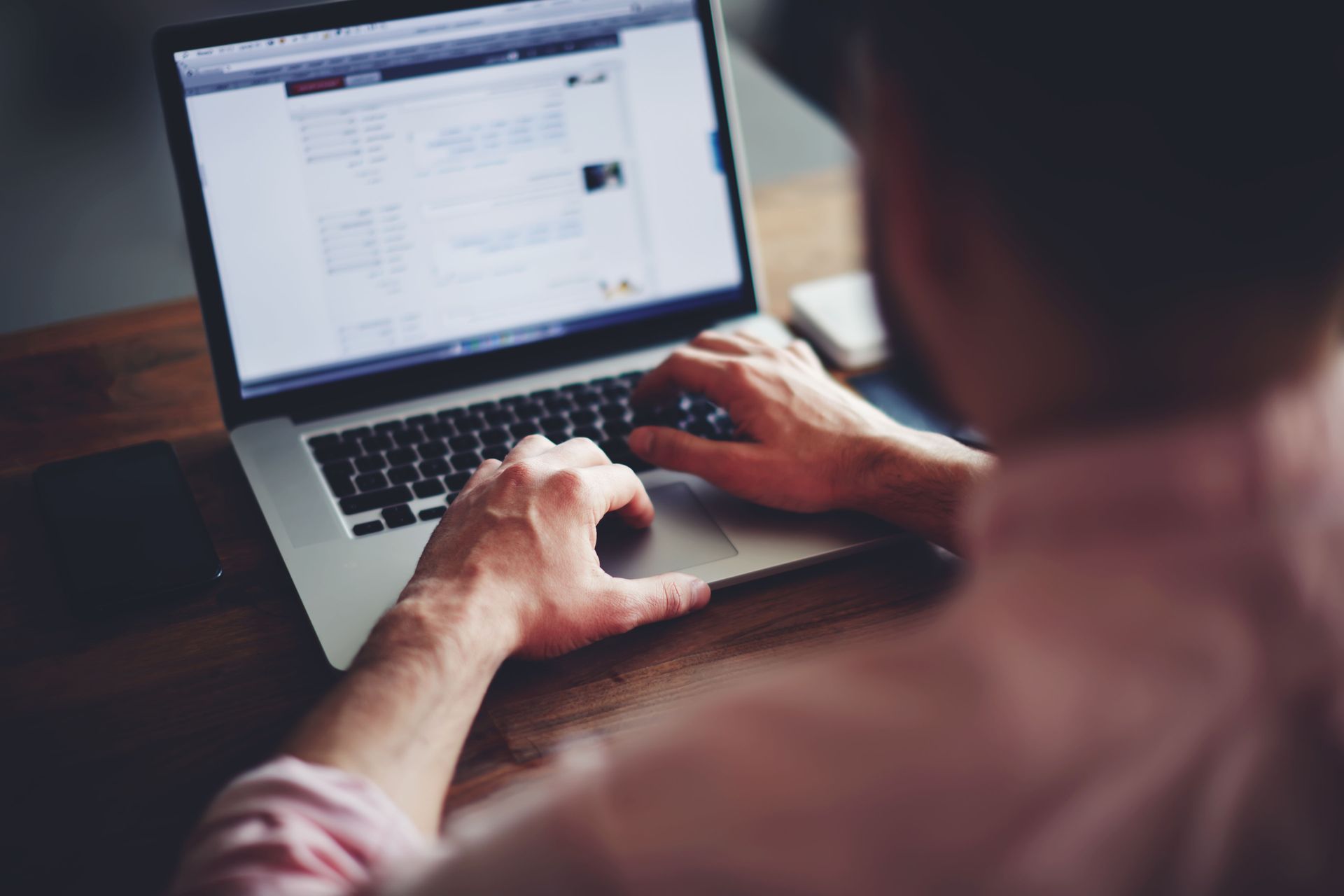 Person typing on a laptop at a desk, with a blurred computer screen in the background.
