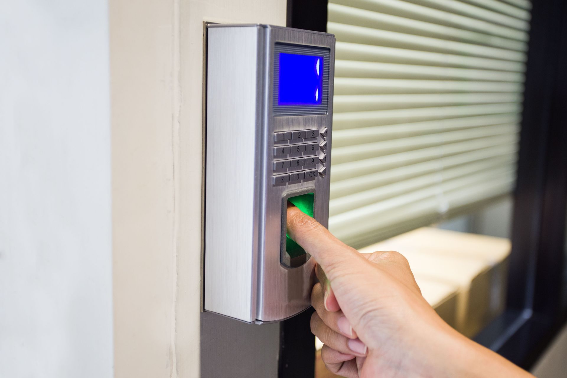 Hand pressing a finger on a biometric access keypad mounted on a wall