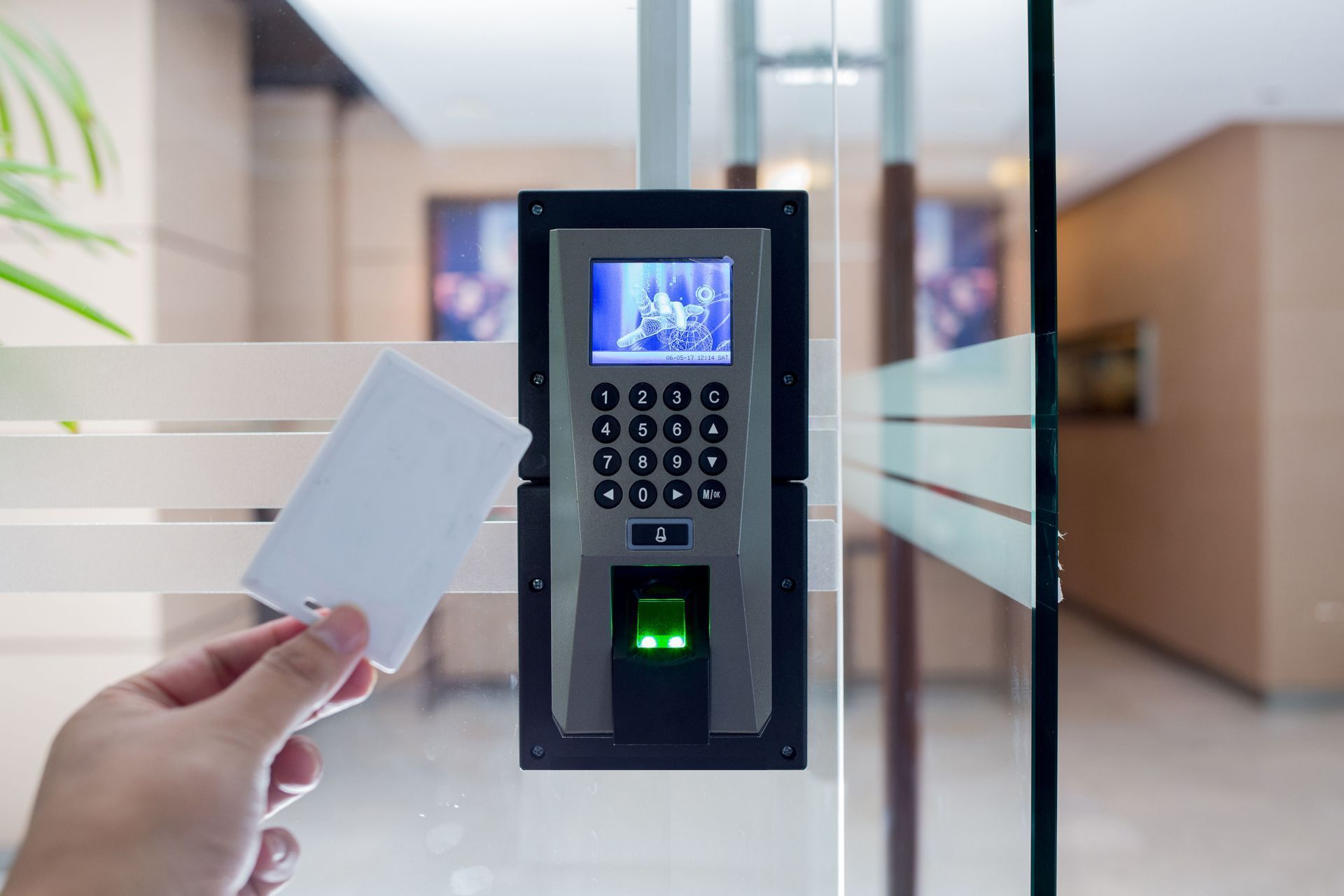 Hand holding access card near biometric keypad at a glass office door