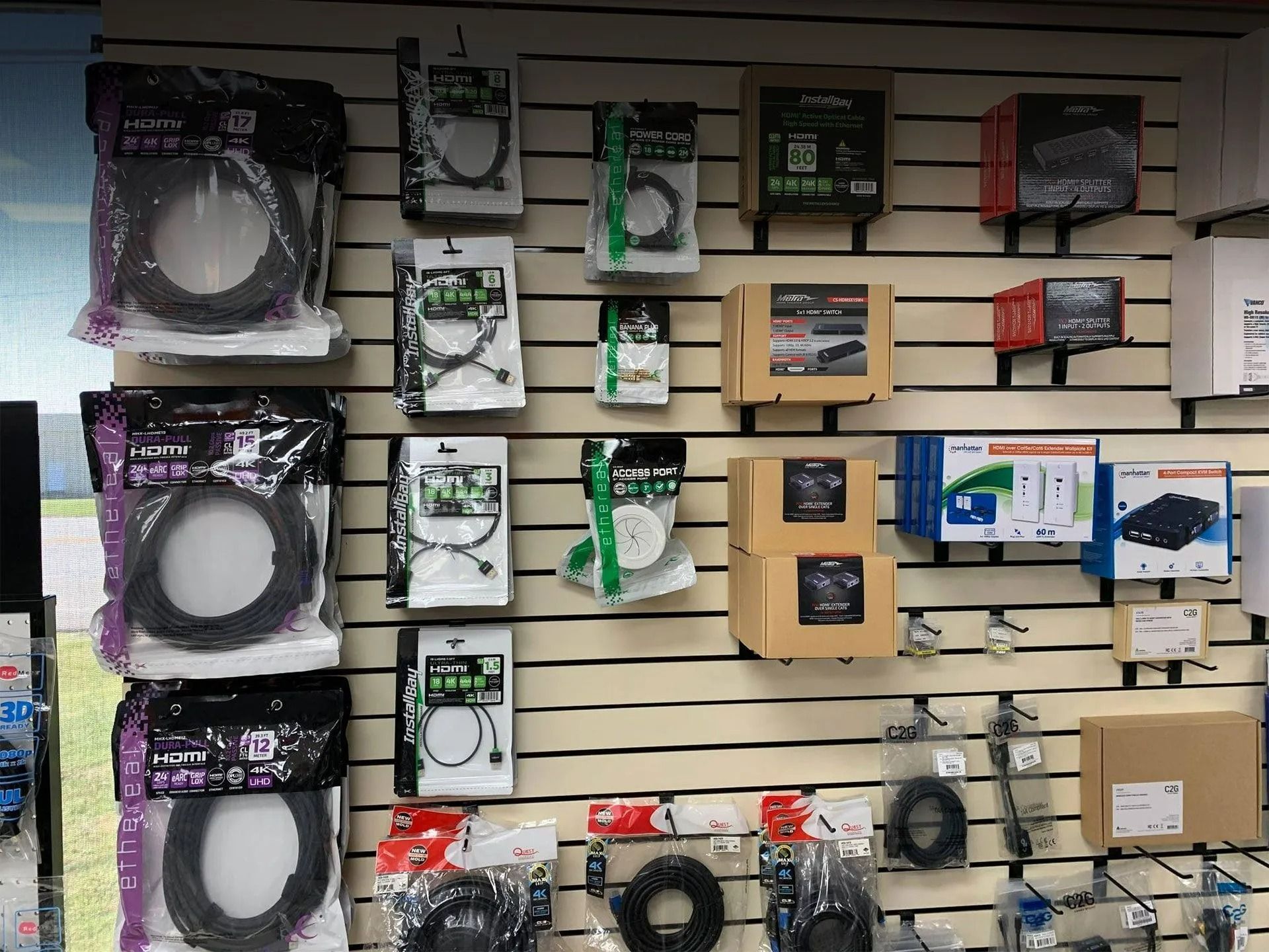 Wall display of assorted electronics accessories in boxed packaging, mostly black, green, and silver.