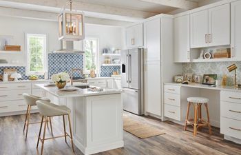 A kitchen with white cabinets , stools , a refrigerator , and a large island.