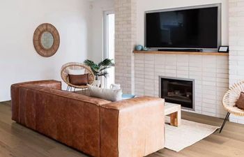 A living room with a brown couch , chairs , fireplace and flat screen tv.