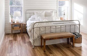 A bedroom with hardwood floors , a bed , nightstands , and a bench.