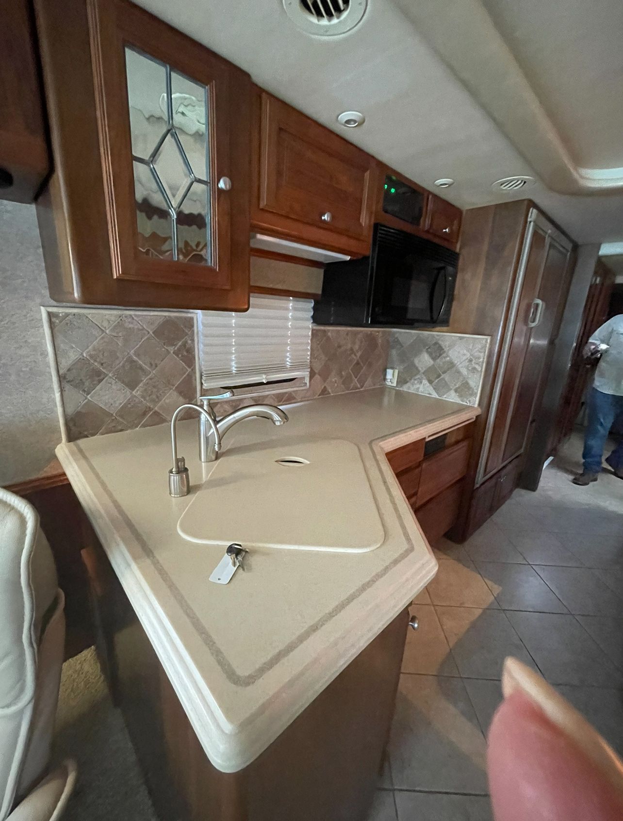 A kitchen in a rv with a sink , refrigerator , microwave and cabinets.