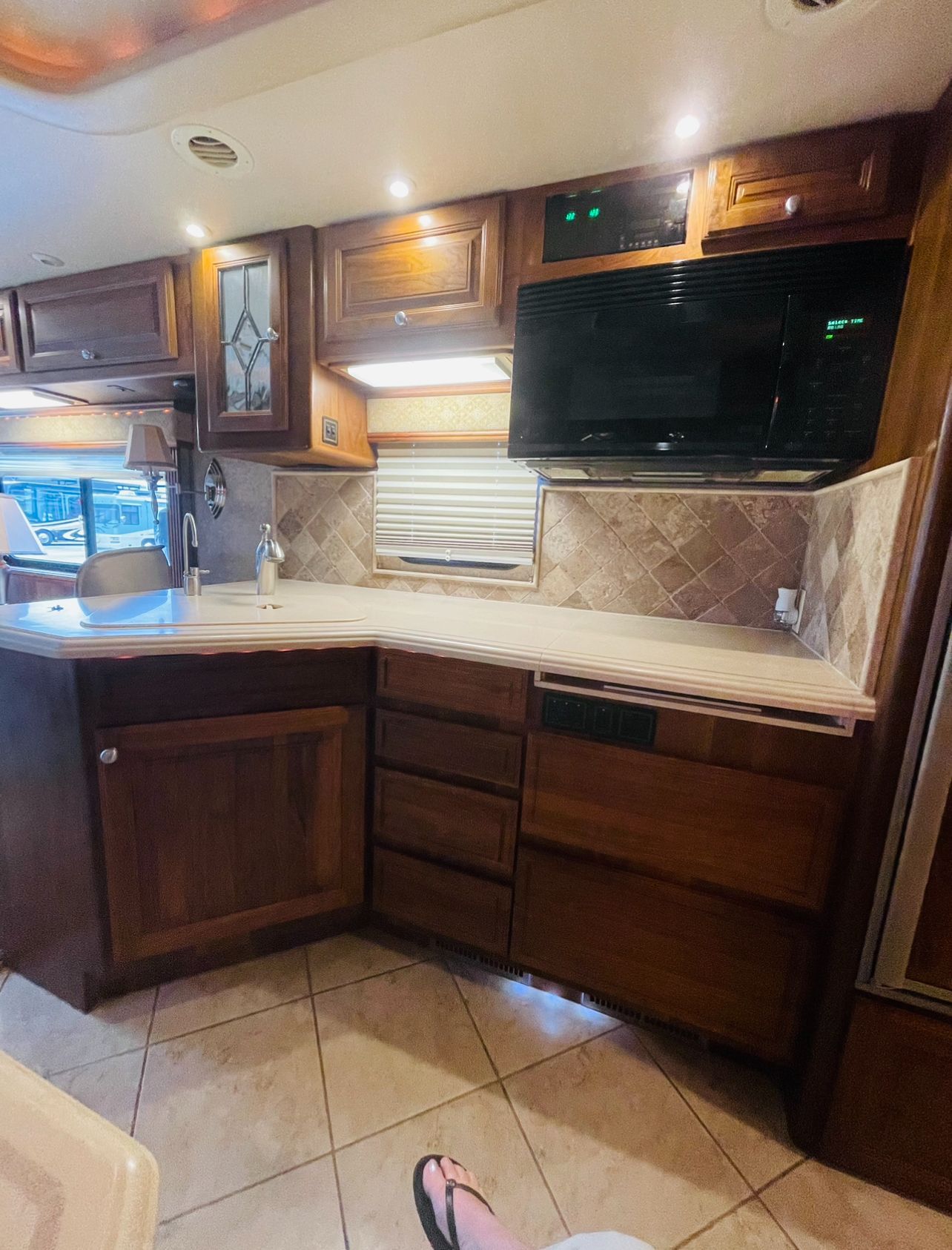 A person is sitting in a kitchen with wooden cabinets and a microwave.