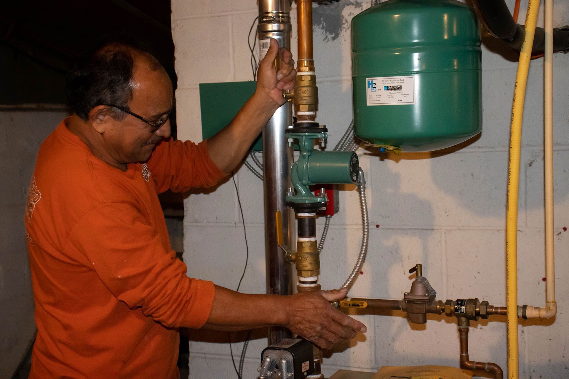 A plumber in an orange shirt is working on a water heater