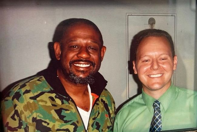 Forest Whitaker with Dr. Pete posing together indoors, one in a camouflage shirt and one in a green shirt with tie.