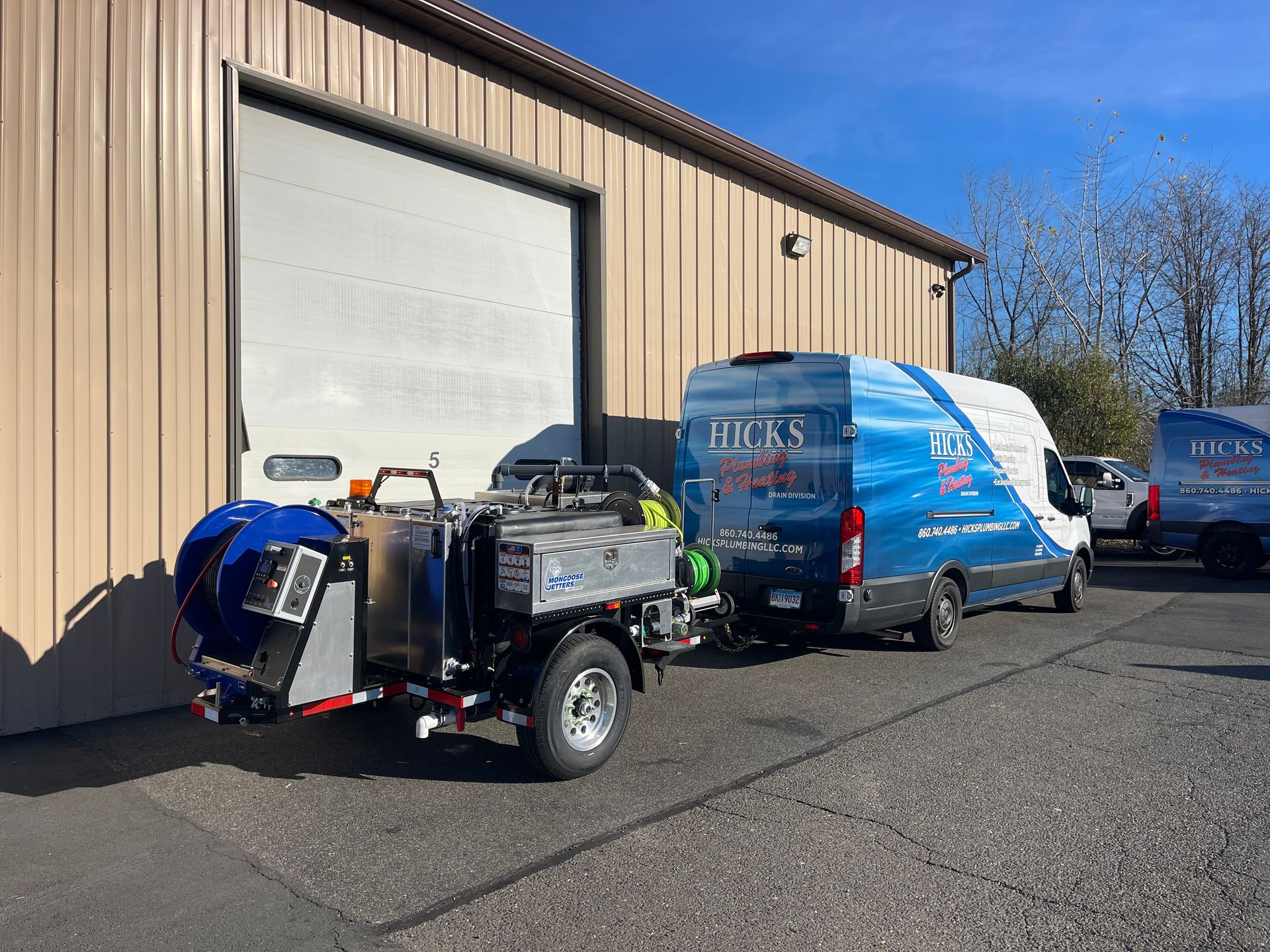 A white van and trailer with blue logos parked in front of a warehouse with its garage door open.
